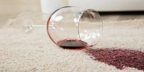 Red wine on carpet adjacent a wine glass lying on carpet